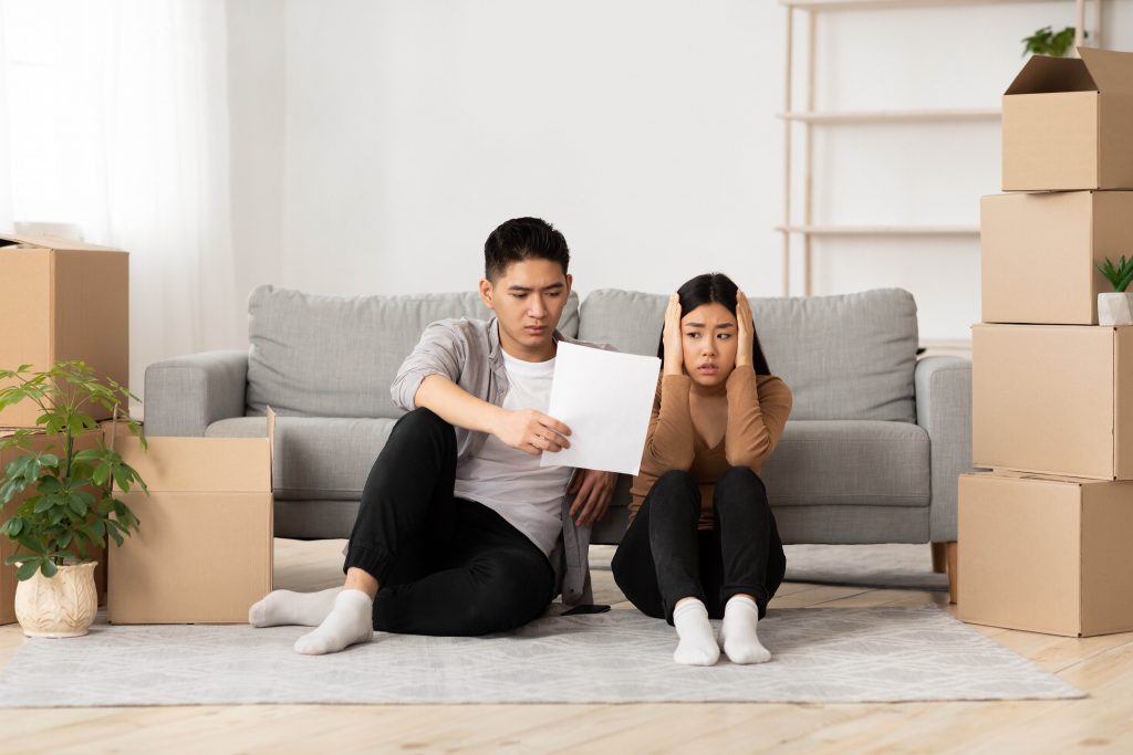 A couple sits on the floor of their apartment, examining what appears to be an eviction notice.